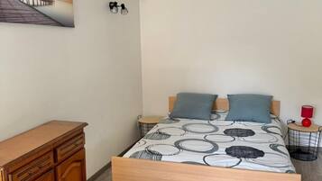 Een slaapkamer met een houten bed, een houten dressoir, een tafeltje en een wandlamp.