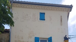 Een gebouw met twee verdiepingen, een witte gevel, een balkon met blauwe luiken en een garagepoort.