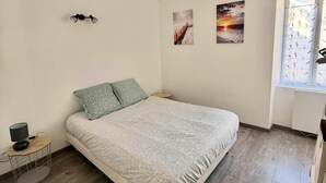 Een slaapkamer met een bed, nachtkastje, lamp en twee decoratieve wandpanelen.