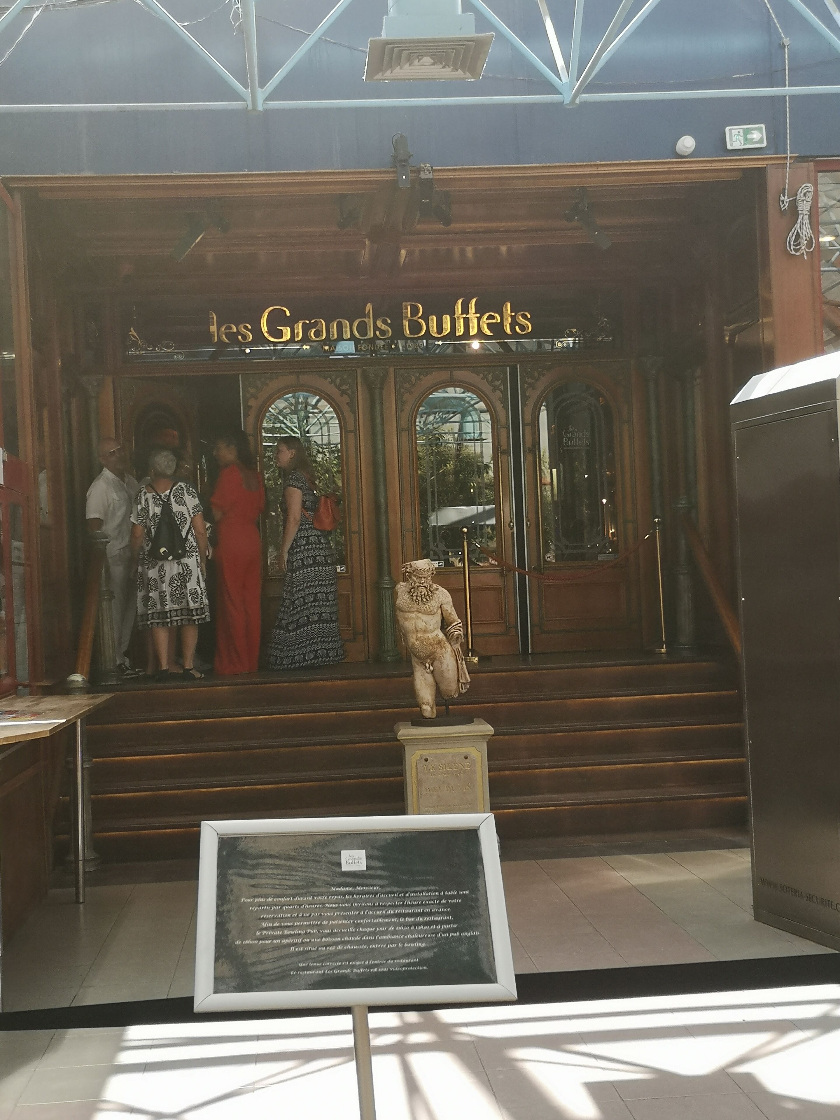 Entrada a Les Grands Buffets con una estatua de una figura sentada y un cartel.