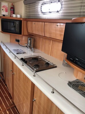 Compact kitchenette with a stove, microwave, and sink, featuring a flat-screen TV.