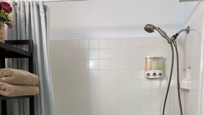 A bathroom with a bathtub, shower, toilet, and a shelf with towels. - Private Room on Serene Property in Hilo (Hilo)