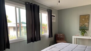 A bedroom with a bed, a chair, a desk, a window with curtains, and a painting on the wall. - Private Room on Serene Property in Hilo (Hilo)