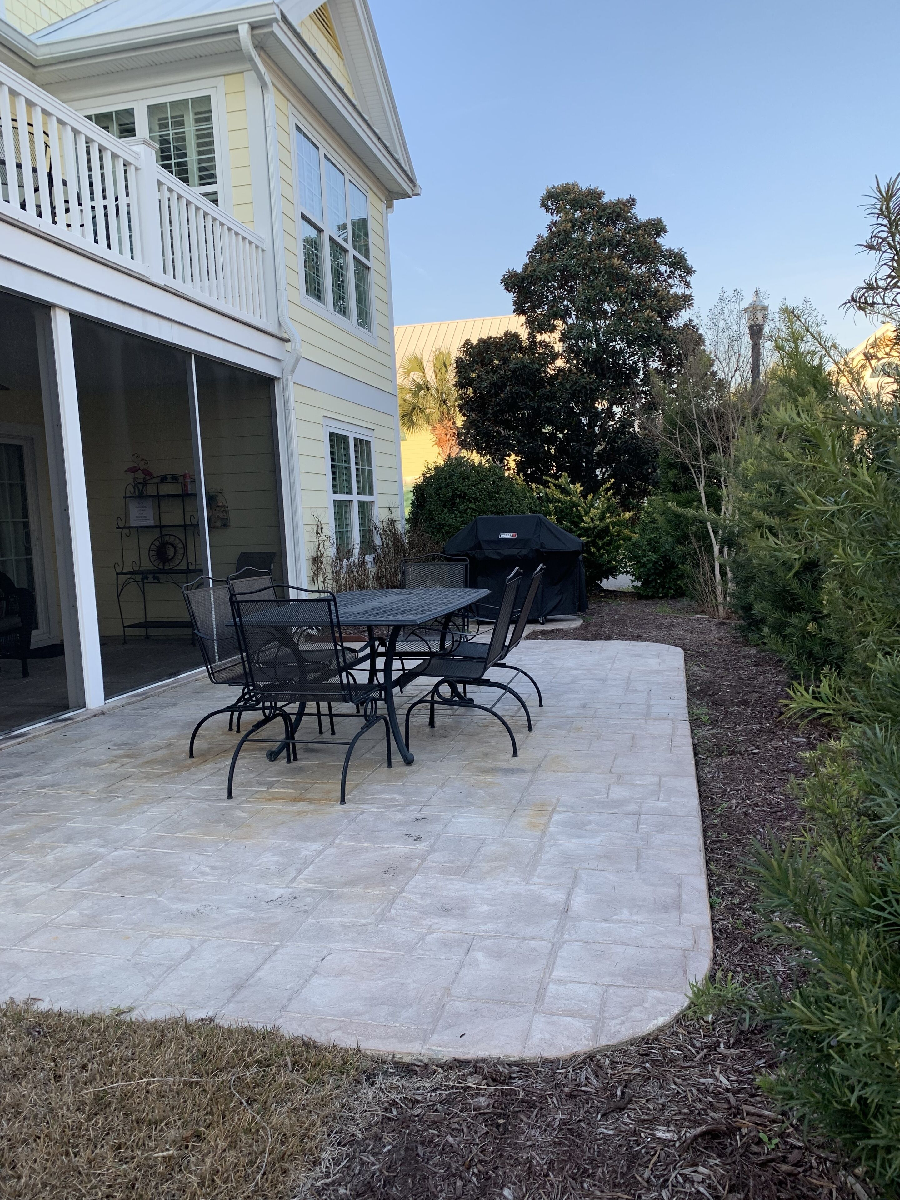 En terrasse med et bord og stole, grill under overdækning, og en bygning med balkon.