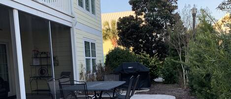 En terrasse med et bord og stole, grill under overdækning, og en bygning med balkon.