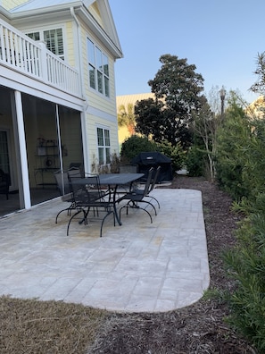 Une terrasse avec une table et des chaises, un barbecue abrité et un bâtiment doté d’un balcon.