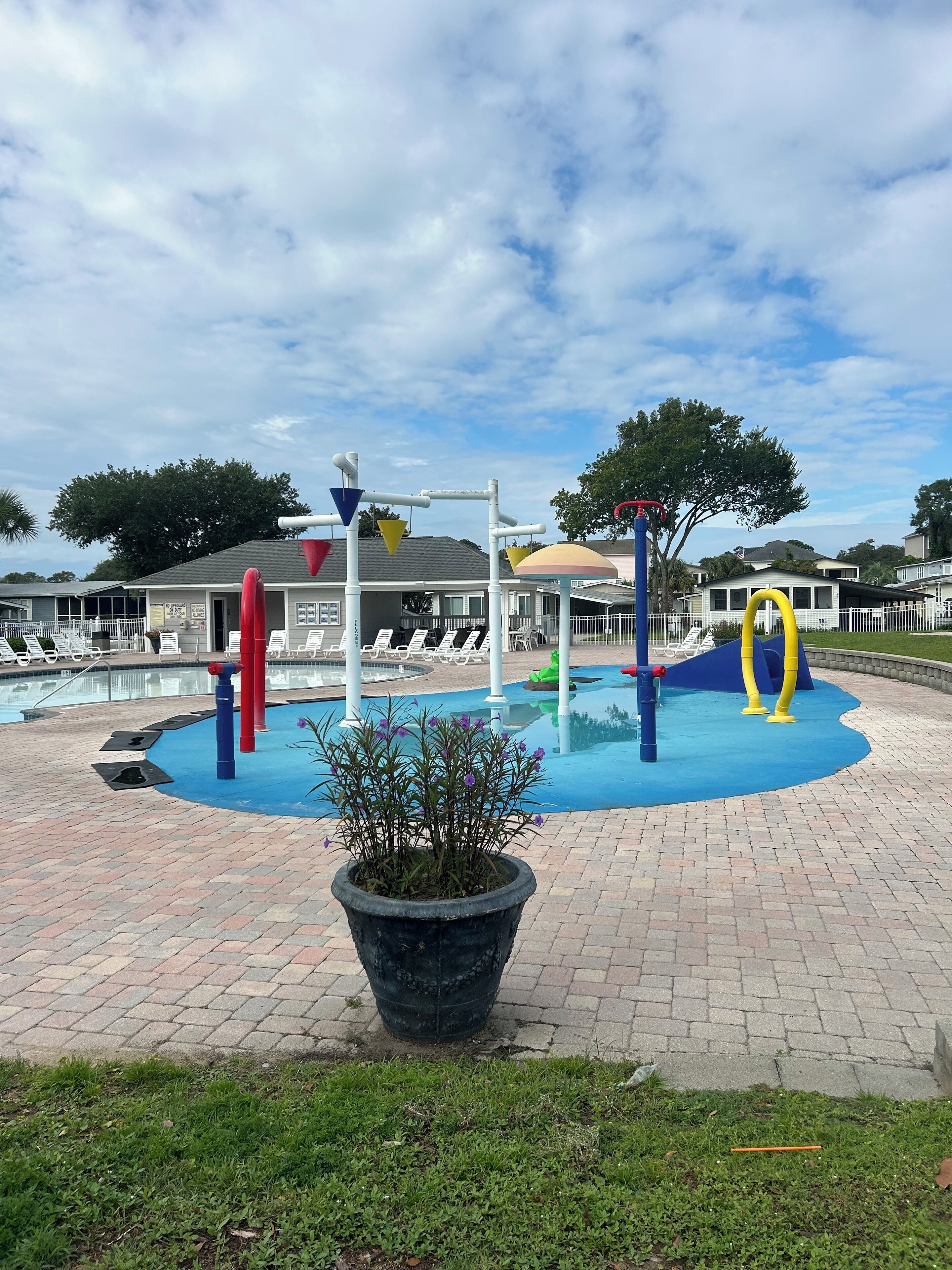 A playground with a pool, lounge chairs, and a large planter in the foreground.