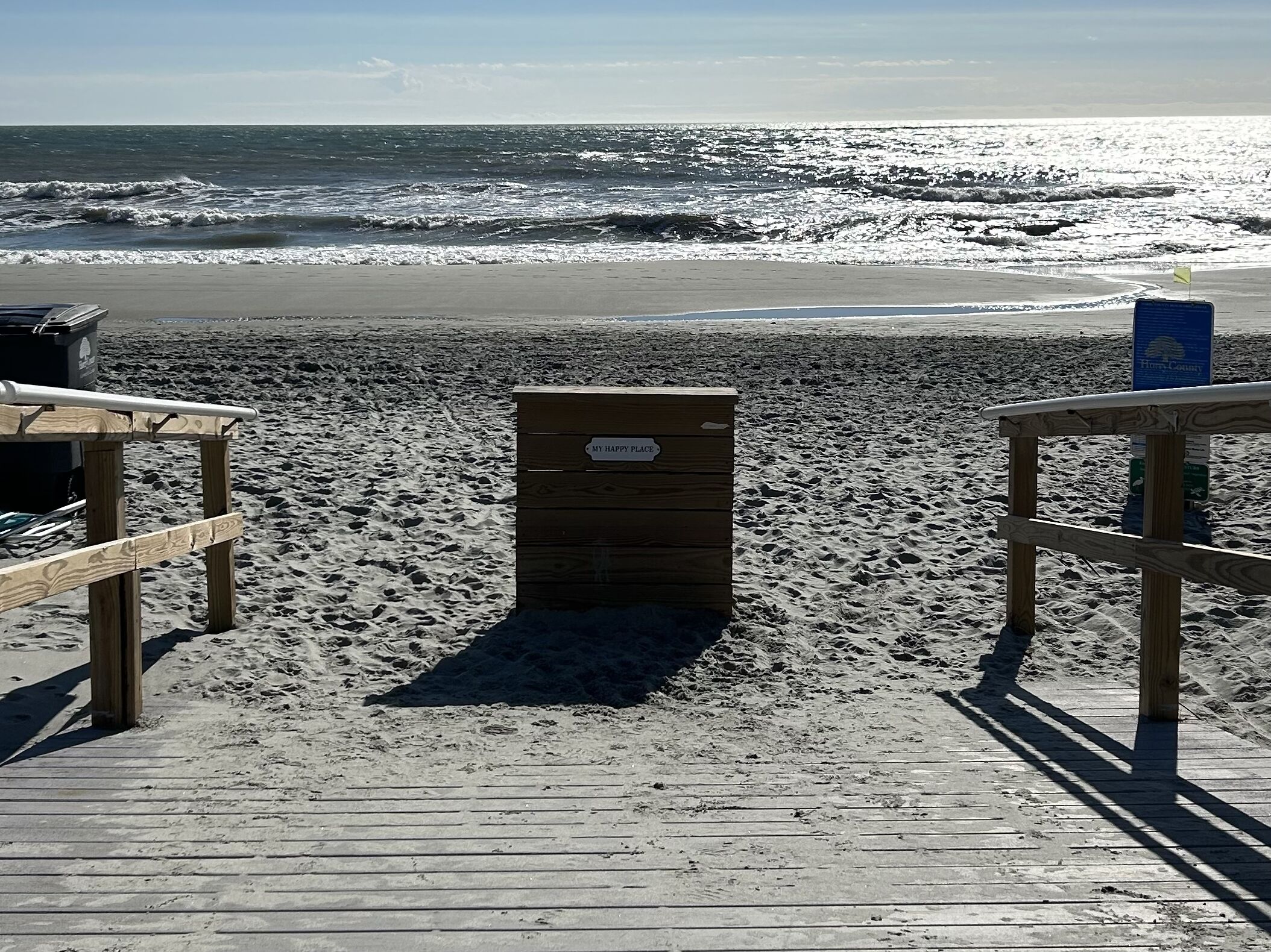 A wooden beach boardwalk leading to a beach with a sign reading "MY HAPPY PLACE".