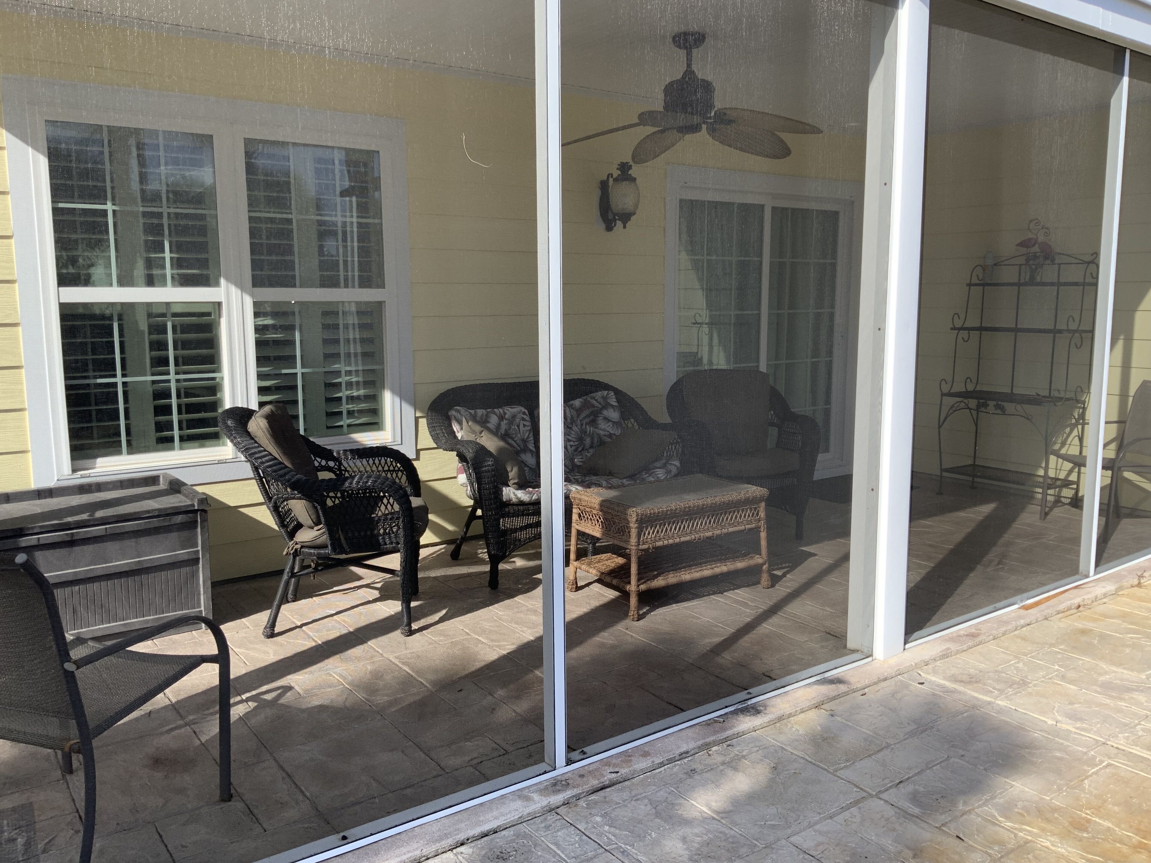 A covered patio with wicker furniture, a ceiling fan, and a metal table.
