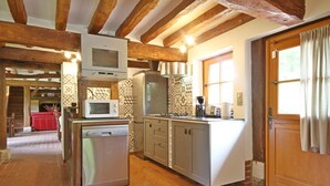 Une cuisine compacte équipée d’un micro-ondes, d’un réfrigérateur et d’un lave-vaisselle intégrés. Elle se distingue par ses poutres apparentes en bois et son sol en briques.