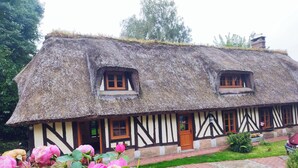 Une maison de campagne traditionnelle, avec un toit de chaume, un toit à pignon et un petit porche.