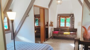 Une chambre à coucher avec un lit, un plancher en bois, une fenêtre, un miroir et un ours en peluche.