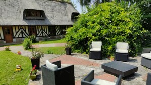 Une terrasse dotée de meubles en osier, un bâtiment au toit de chaume et une végétation luxuriante.