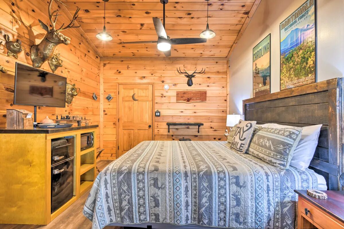 A rustic cabin-style bedroom with a bed, a wooden headboard, a mounted television, and a wooden cabinet with a sink.