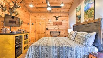 A rustic cabin-style bedroom with a bed, a wooden headboard, a mounted television, and a wooden cabinet with a sink.