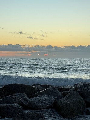 Escena costera con olas, rocas y un atardecer.