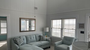 Un salón espacioso con un sofá seccional azul claro y un sillón a juego, paredes blancas y ventanas grandes con persianas.
