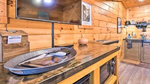 Un interior de madera con una zona de bar, un televisor montado en la pared y una encimera de cocina con electrodomésticos.