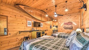 Una cabaña con paredes y techo de madera, dos camas con ropa de cama a cuadros, una kitchenette y un televisor montado.