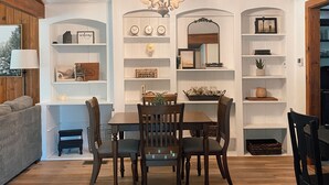 A dining area with a wooden table and chairs, surrounded by white shelving with various decorative items. - Sequoia Escape . Close to The  Springville Ranch Venue & Sequoia Nat. Park. (Springville)