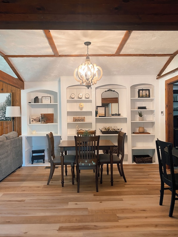 A dining area with a wooden table and chairs, surrounded by white shelving with various decorative items.