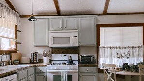 A kitchen with white cabinets, a microwave, a stove, and a dining area with a table and chairs. - Sequoia Escape . Close to The  Springville Ranch Venue & Sequoia Nat. Park. (Springville)
