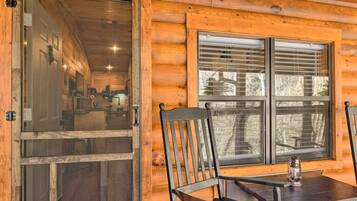 A wooden cabin interior with a dining table, chairs, and a window with blinds.