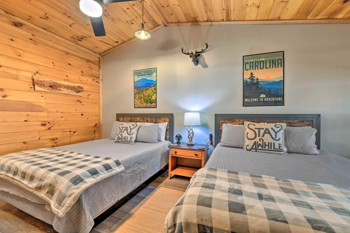 A room with two beds, wooden walls, a mounted deer head, and two posters on the wall.