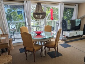 A dining area with a glass table, wicker chairs, a red bowl, and a television in the background.
