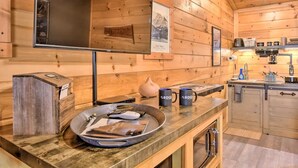 A wooden cabin interior with a kitchen area, wooden walls, and a large mirror.