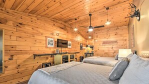 A cozy cabin-style room with two beds, wooden walls, a kitchenette, and a ceiling fan.