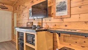A wooden cabin interior with a kitchen area, a mounted flat-screen TV, and framed pictures on the walls.