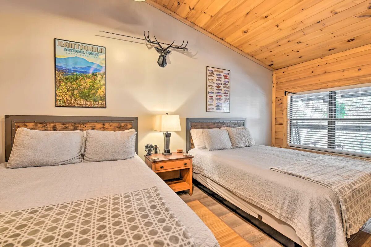 Ein Zimmer mit zwei Betten, einer Holzbalkendecke, einem Nationalparkplakat und einem an der Wand befestigten Hirschkopf.