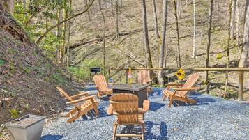 An outdoor seating area with wooden chairs and a table, surrounded by gravel and trees.