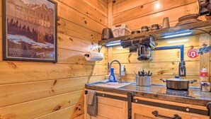 A wooden cabin interior with a kitchen area featuring a stove, sink, and a framed poster on the wall.