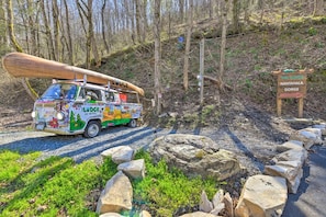 A colorful bus parked at a campsite with a large canoe on top, surrounded by rocks and trees.