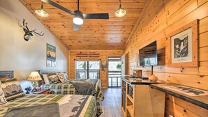 A cabin interior with two beds, a kitchenette, and a ceiling fan.
