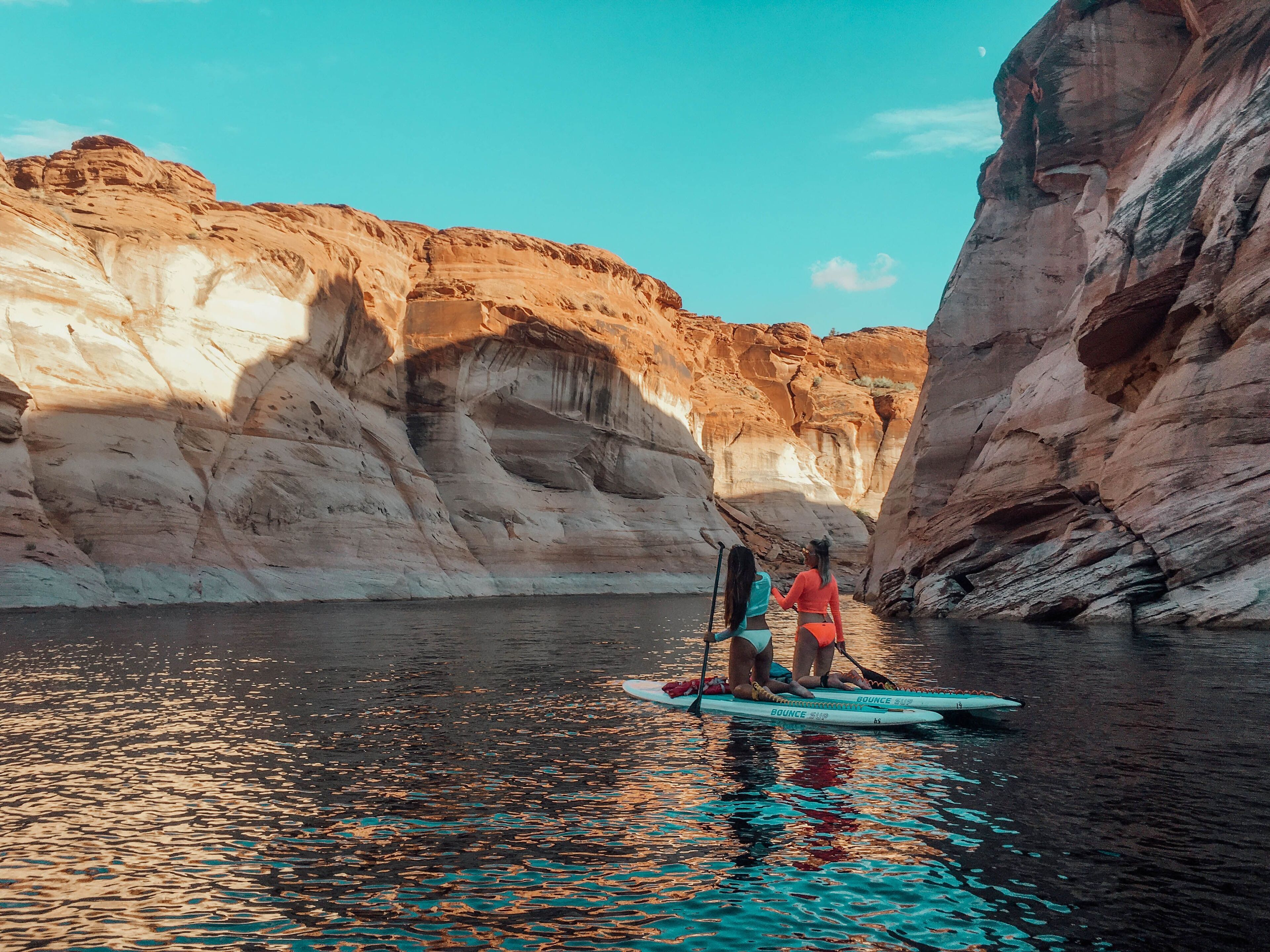 Two people paddleboarding in a canyon with rocky cliffs.