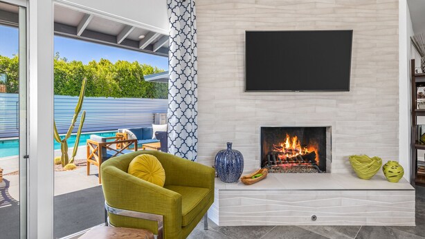Ein modernes Wohnzimmer mit Kamin, Flachbildfernseher und Blick auf einen Pool durch Glastüren.
