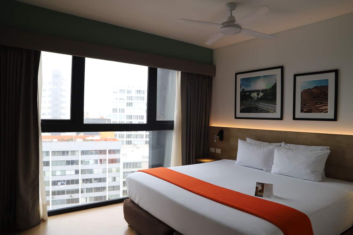 A hotel room with a large bed, a ceiling fan, a window with curtains, and two framed pictures on the wall.