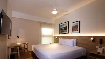 A hotel room with a bed, desk, chair, ceiling fan, and two framed pictures on the wall.