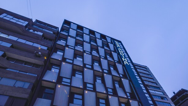 A modern hotel with a glass facade, multiple floors, and a well-lit entrance with steps leading up to the doors. - Casa Andina Standard Benavides (Lima)
