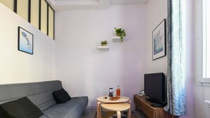 Un salon moderne avec un canapé gris, une petite table ronde sur laquelle se trouve une boisson, un téléviseur posé sur un meuble en bois et un sol à motifs.