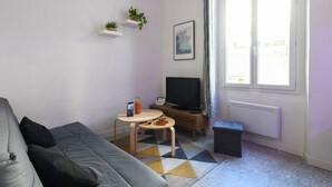 Un salon avec un canapé, une petite table sur laquelle se trouve une bouteille, un téléviseur et une fenêtre avec des rideaux.