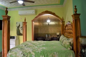 A bedroom with a bed, a ceiling fan, an air conditioning unit, a decorative arch, and a small table with a statue.