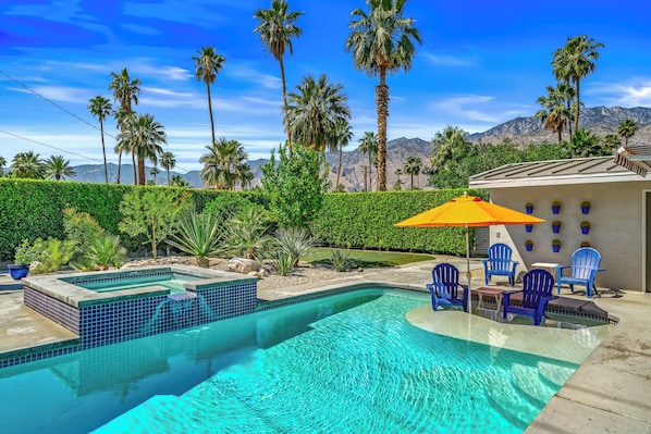 A swimming pool with a hot tub, surrounded by palm trees and a mountain backdrop.