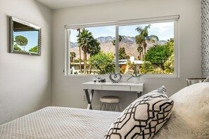 Ein Schlafzimmer mit einem Bett, einem Schreibtisch, einem Stuhl, einem Fenster mit Bergblick und einem Spiegel.