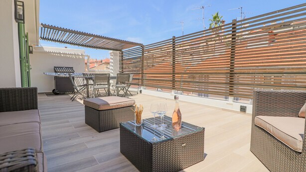 A rooftop patio with wicker furniture, a glass-top table with wine glasses and a bottle, and a pergola structure. - Rooftop design apartment Cannes (Cannes)