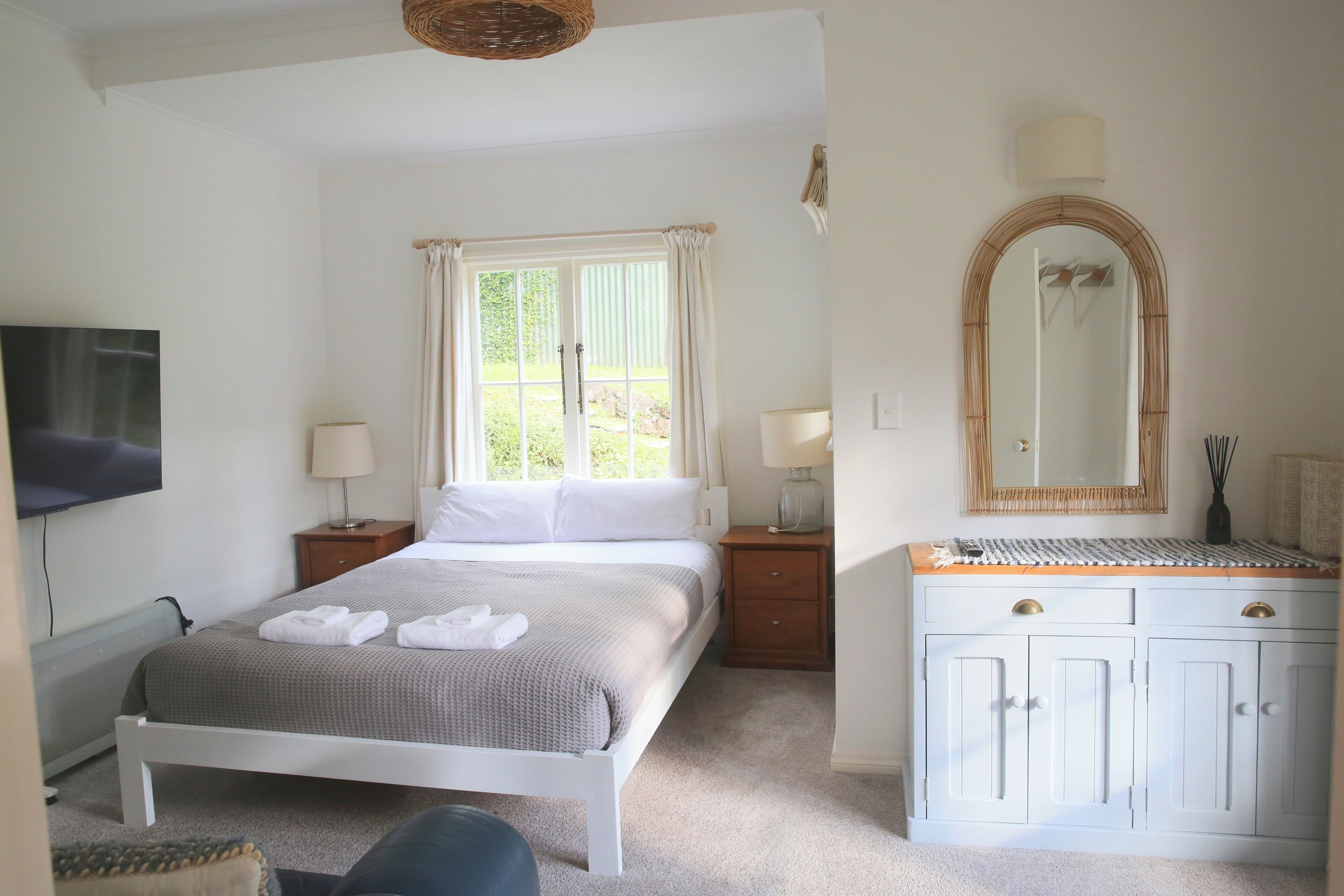 Une chambre à coucher comprenant un lit, des tables de chevet, une télévision, une fenêtre avec des rideaux, un miroir et une armoire.
