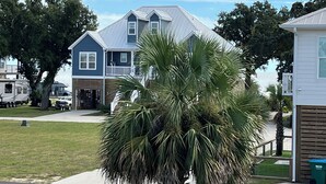 Une maison à deux étages avec un balcon, une pelouse et un palmier au premier plan.